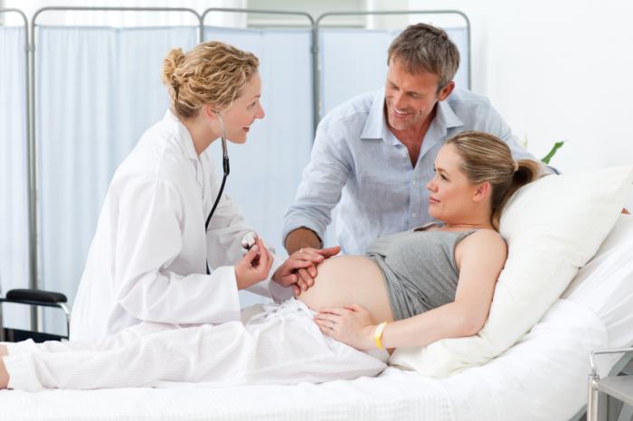smiling pregnant woman with partner and doctor in hospital bed